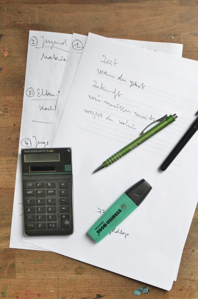 Top view of office stationery including calculator, papers, pen, and marker on a wooden desk.